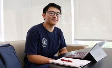 Hope Scholar Tytain Sun in Cybersecurity Camp t-shirt at desk with computer, notebook, and pen